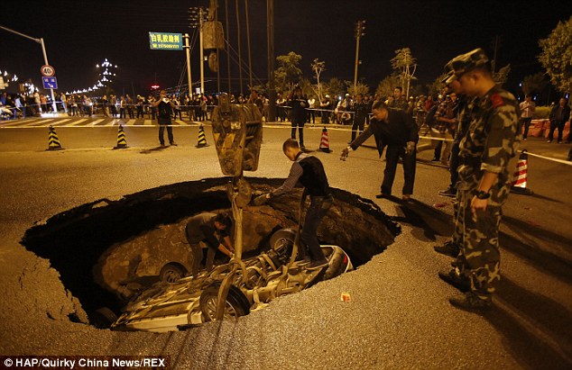 Officials attach a hoist to the car's chassis and begin the process of hauling it out of the sinkhole
