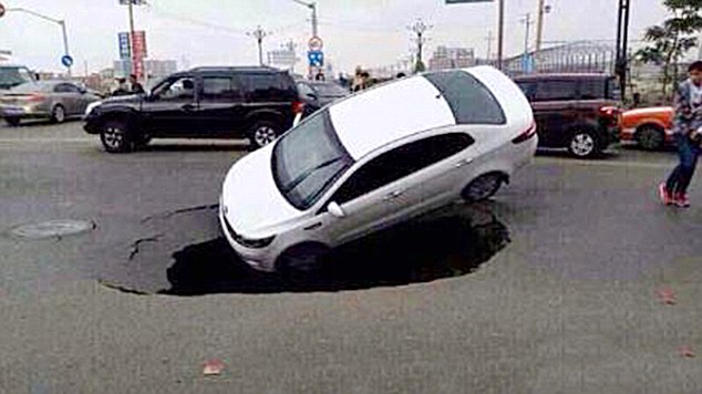 The car teeters on the edge of the hole and begins to flip on its side as the sinkhole begins to widen