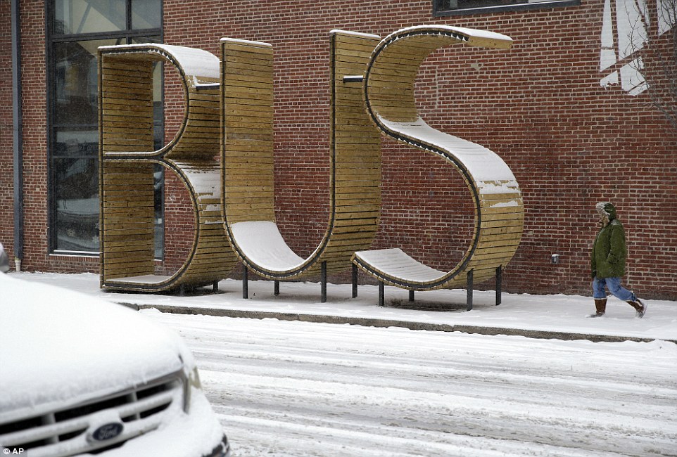 A woman walks past an empty bus stop as a light snow falls Tuesday in Baltimore