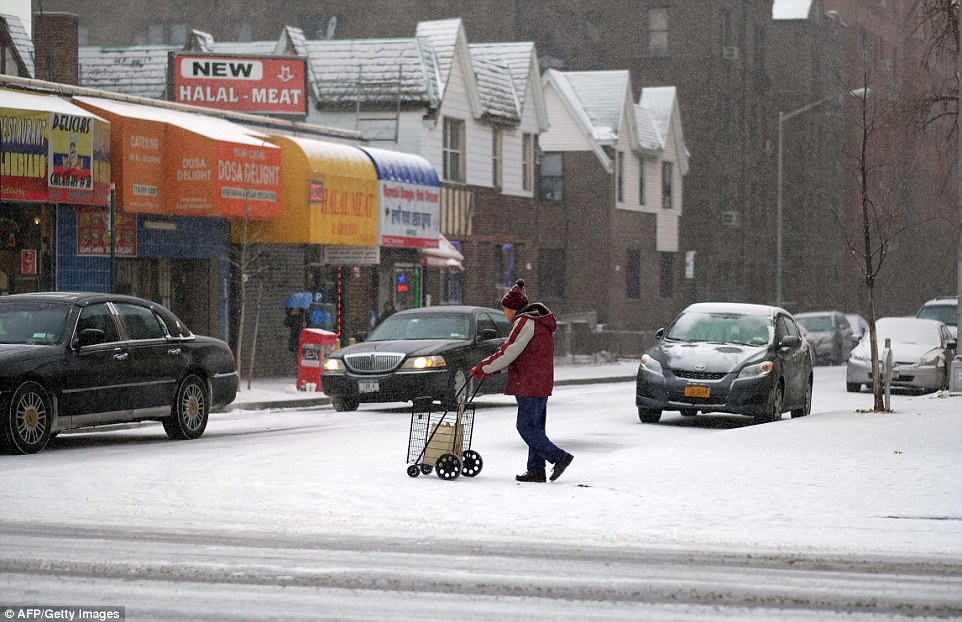 A man crosses a street with his grocery cart during a snowfall in New York's borough of Queens on January 6, 2015 as extreme cold gripped Canada and northern parts of the US, prompting calls for residents to stay indoors amid increased risks of frostbite and hypothermia