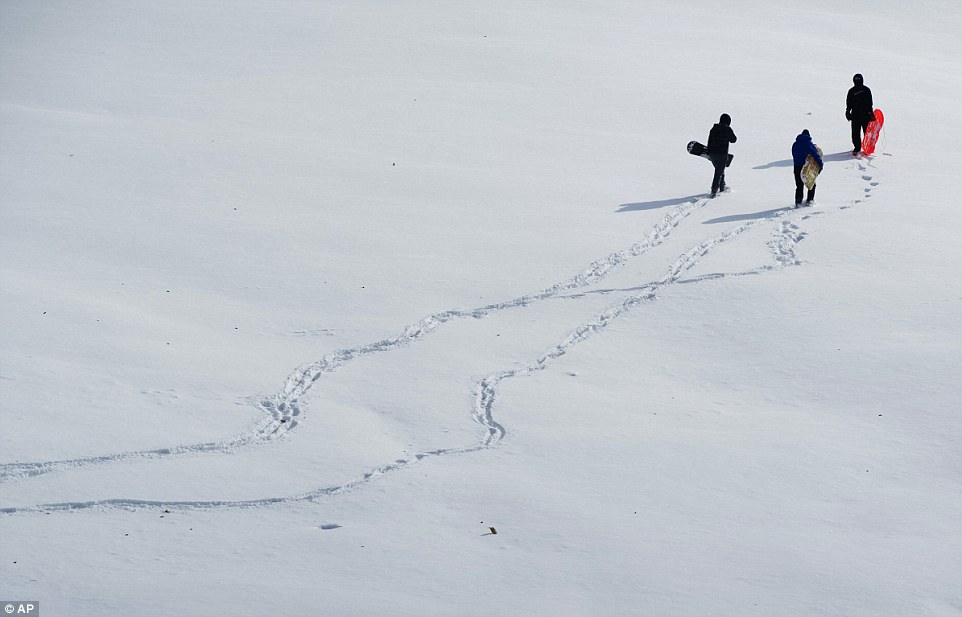 Sledders, from left, Kaitlin Crawford, Casey Brugh and Kyle LeBarron trek across the snow-covered Helfrich Hills Golf Course in Evansville, Indiana in search of the perfect hill on Monday morning