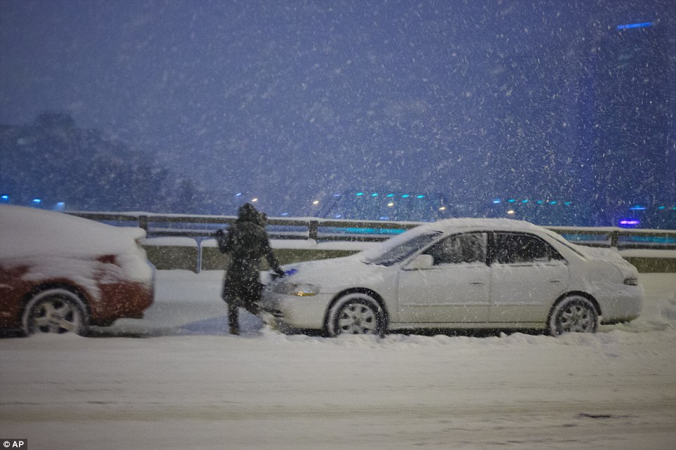 Stranded: This driver in Grand Rapids, Michigan, cleans her car off in the hope of keeping on despite huge quantities of snow falling