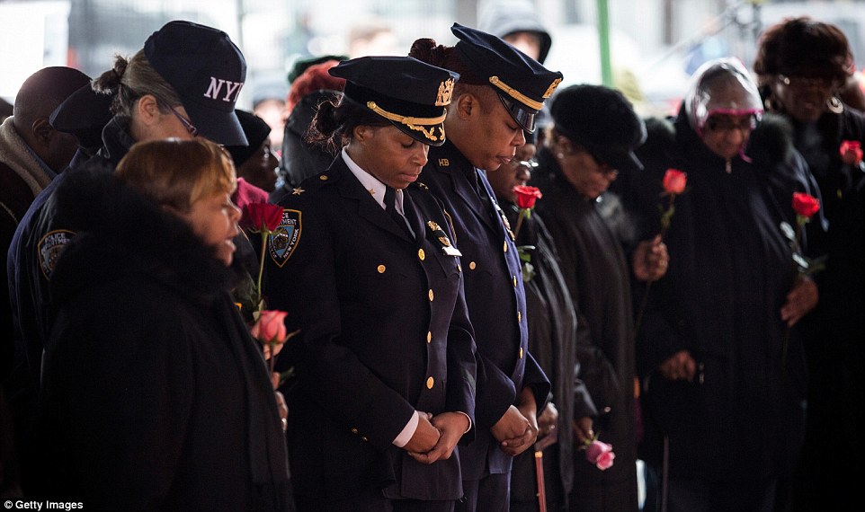 Standing together: Three NYPD officers bow their heads, surrounded by members of the public holding roses