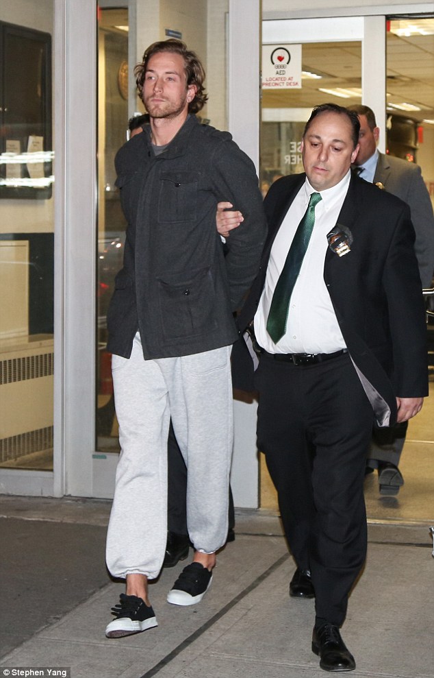 Behind bars: Tommy seen being escorted into Manhattan Central booking by a police officer 